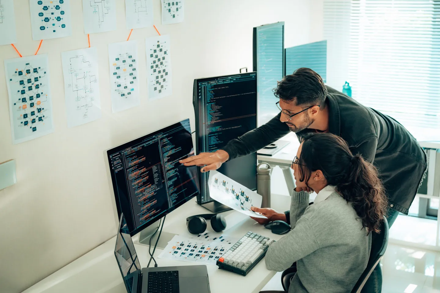 Programmers collaborate on software in front of multiple computer screens.