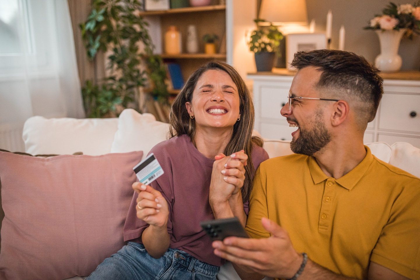 A loving couple checks their home finances using a credit card and a mobile phone.