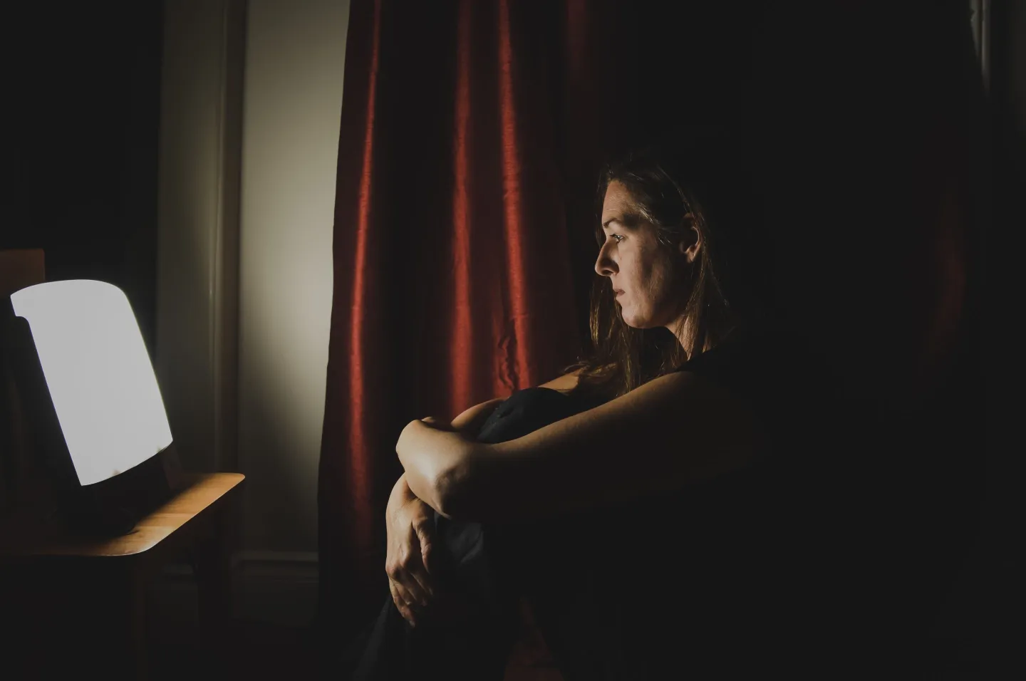 woman sitting in the dark looking at a light-therapy box