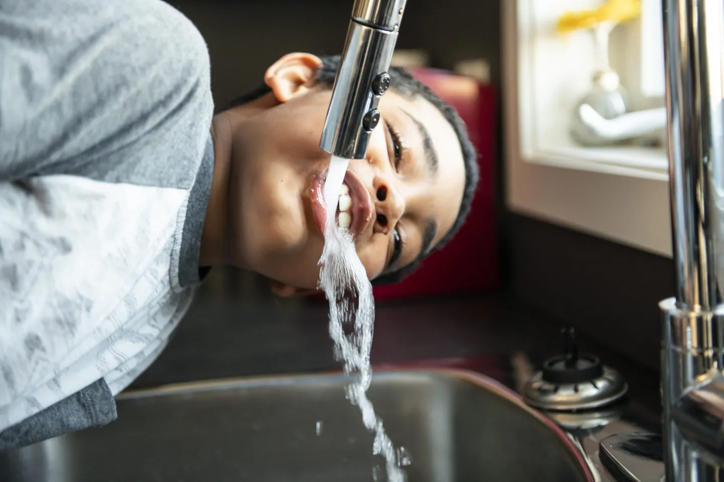 Young boy drinking water right from a sink tap