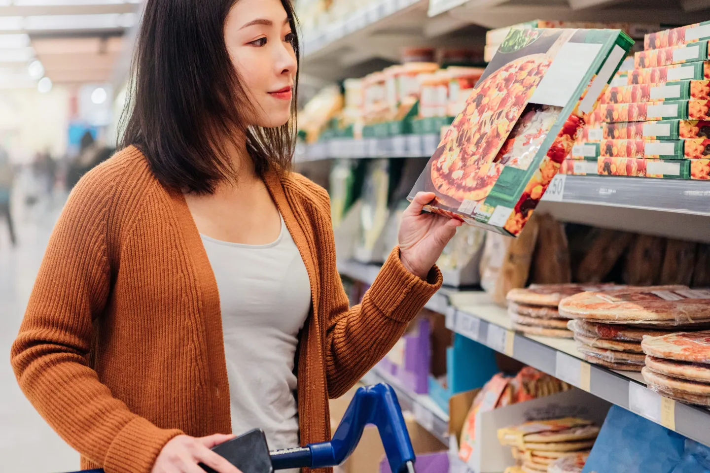 Women in supermarket aisle looking at boxed pizza