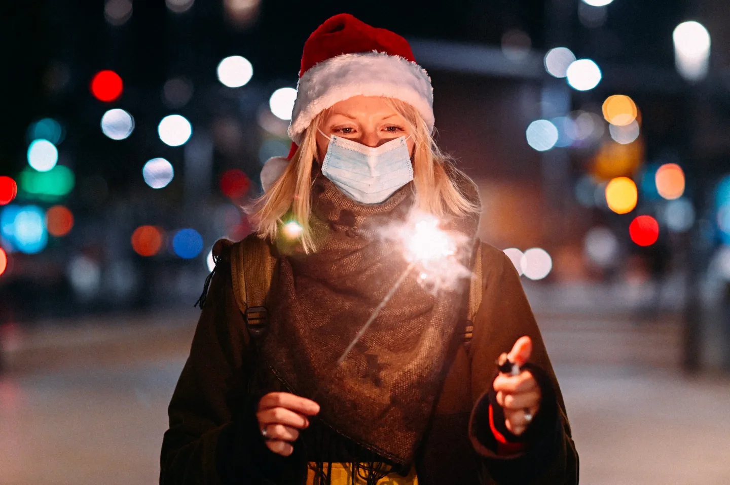 A young woman wearing a face mask holds sparklers while celebrating New Year's Eve.