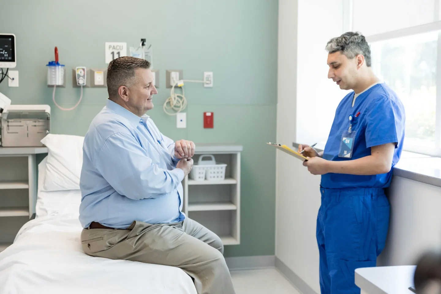 The male patient talks with the nurse and answers questions before seeing the doctor for his symptoms.