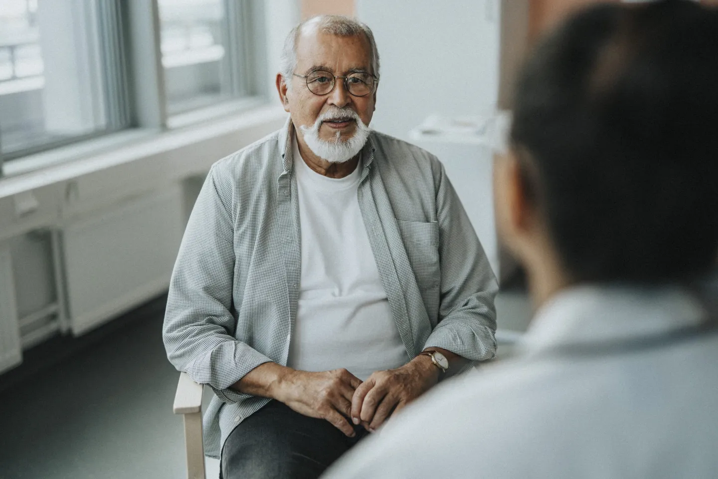 Senior male patient sitting with doctor during consultation at hospital