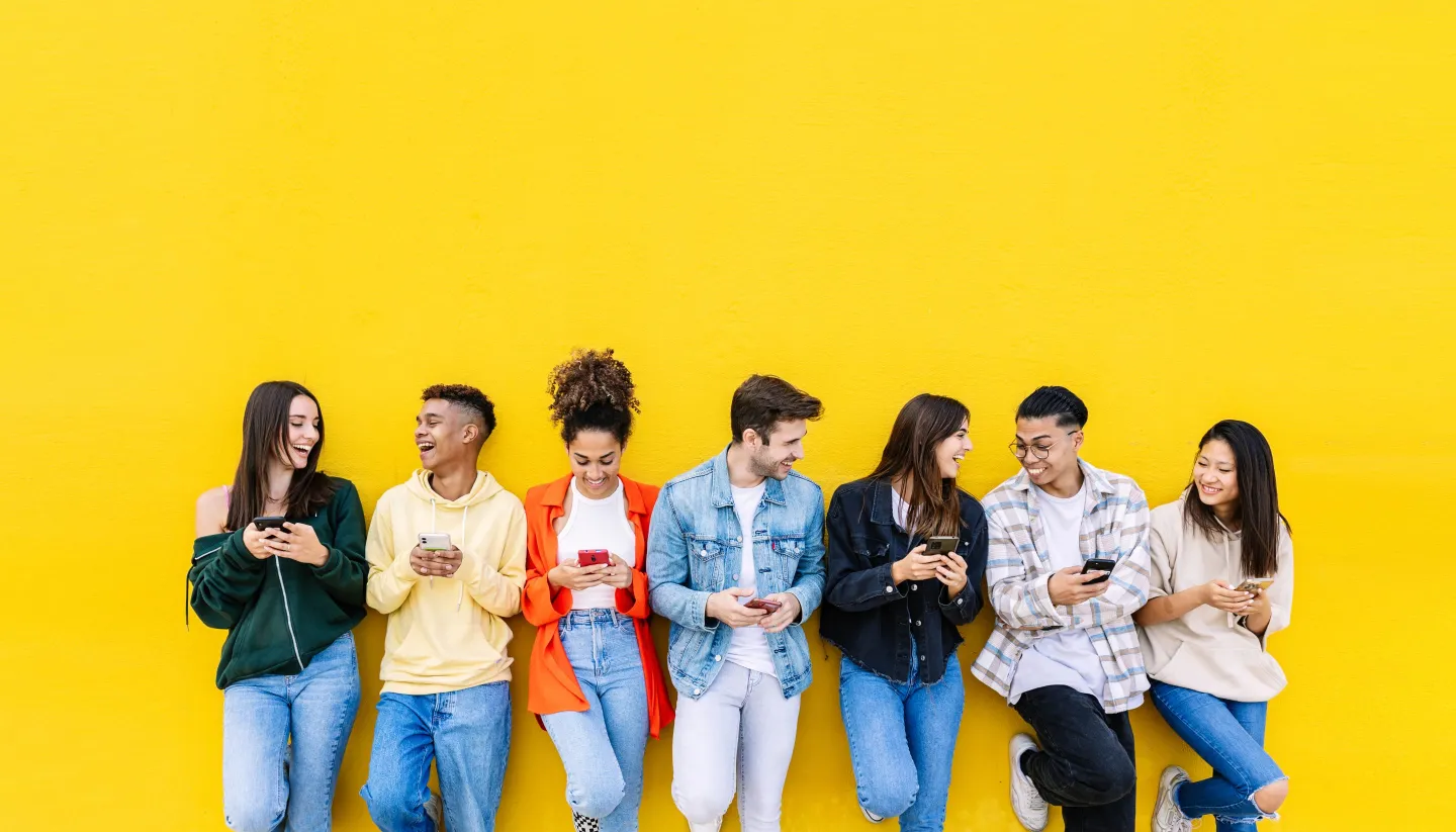 young adults standing against a wall using mobile phones