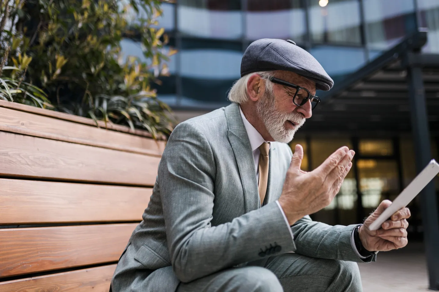 Man with gray hair sitting on a bench and looking at his tablet