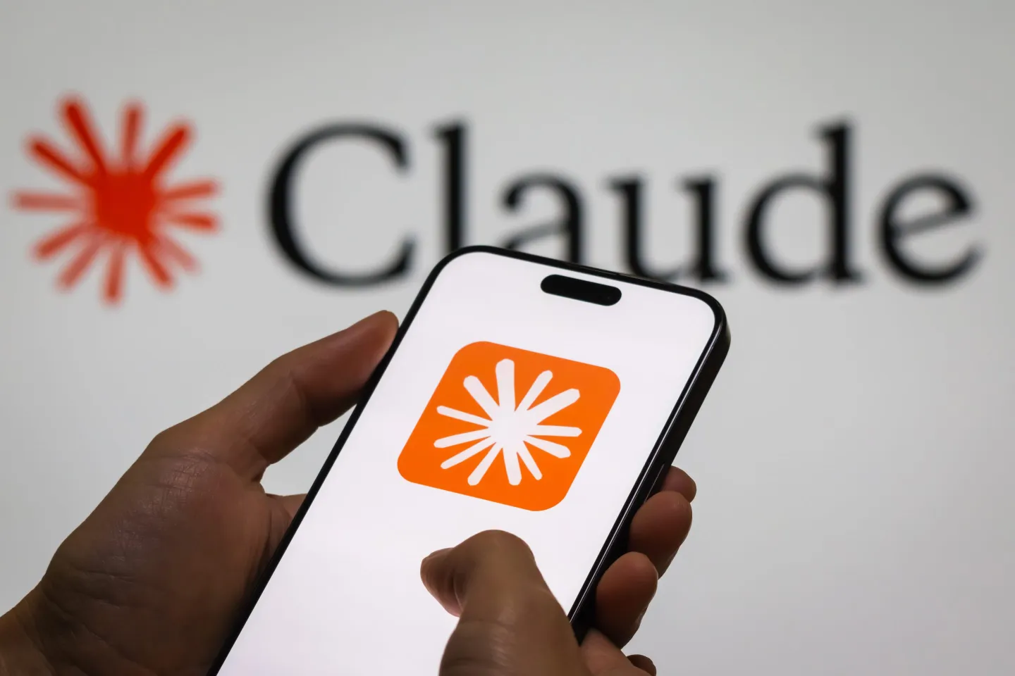 In this photo illustration, a person holds a smartphone displaying the logo of “Claude,” an AI language model by Anthropic