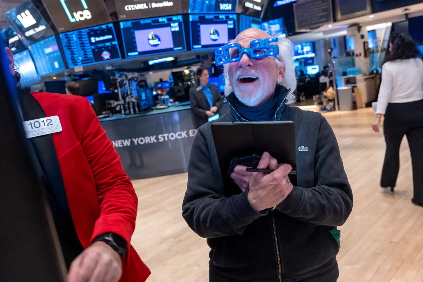 Man with 2025 New Year's glasses smiles on the Wall Street trading floor