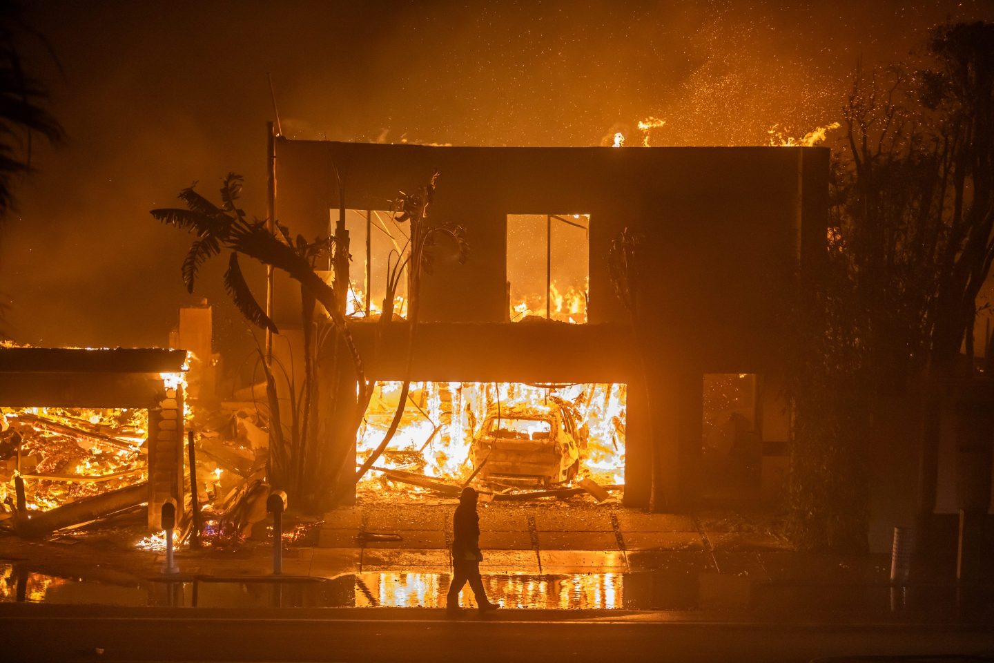 A firefighter watches the flames from the Palisades Fire burning homes on the Pacific Coast Highway