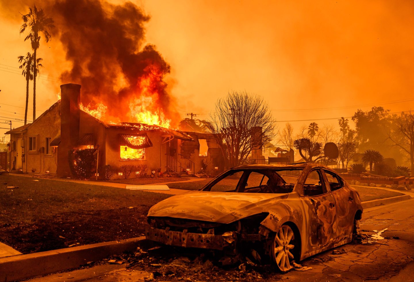 The carcass of a burnt-out car is seen as home burns during the Eaton fire in the Altadena area of Los Angeles county, California