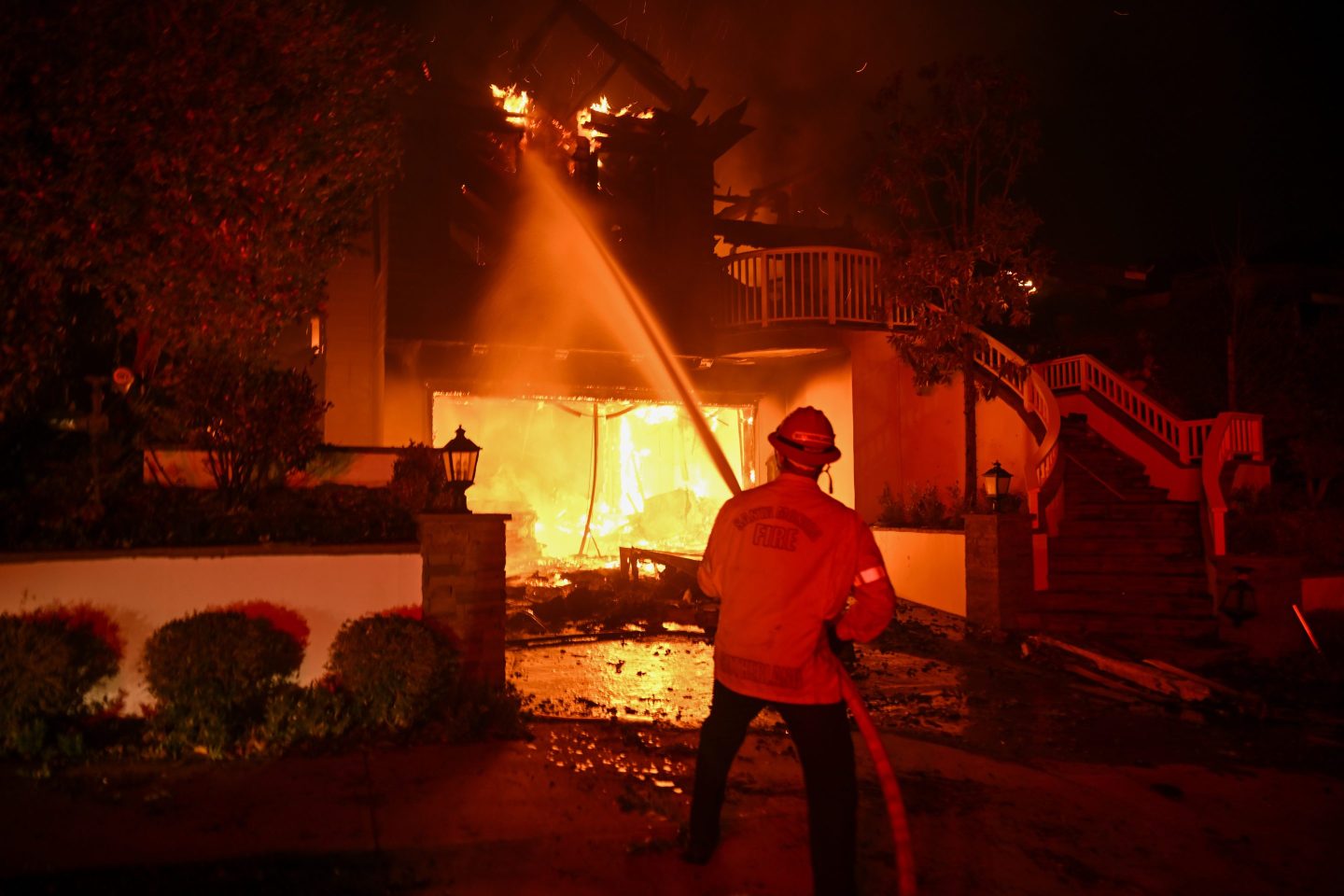 fireman spraying water from a hose at a house on fire