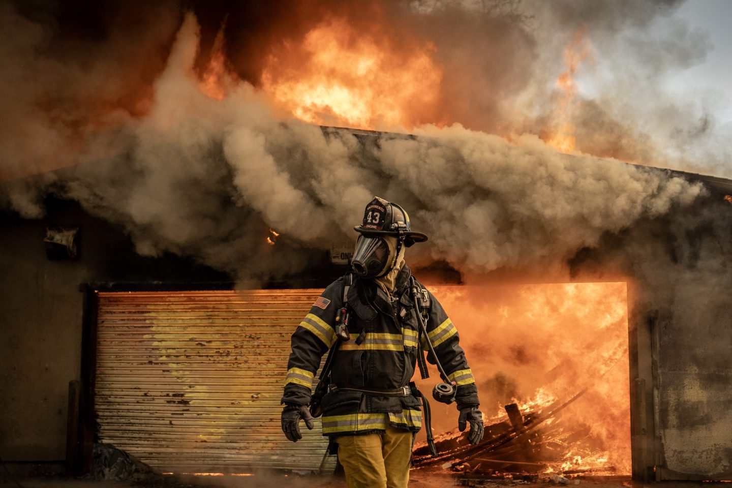 A firefighter in a gas mask in front of a burning structure