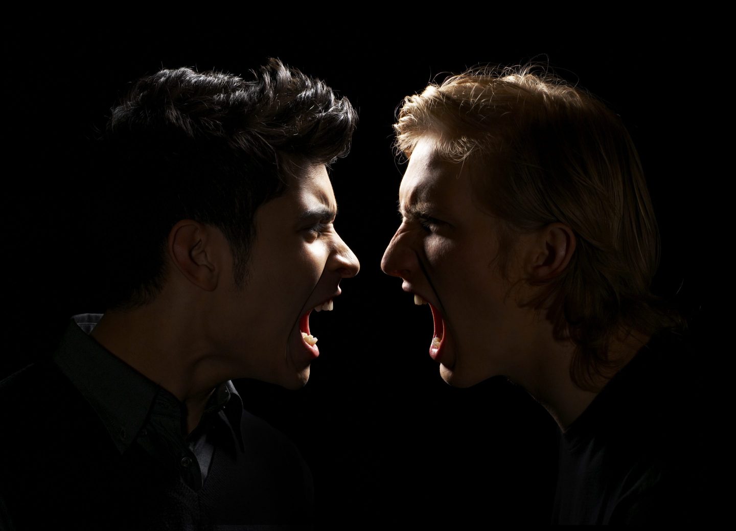 Closeup of men arguing with faces close together on black background