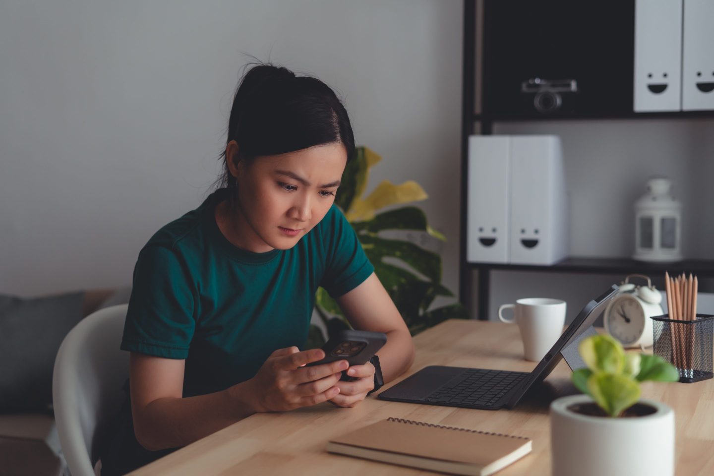 Woman sitting at home office looking at smartphone screen and having problem.