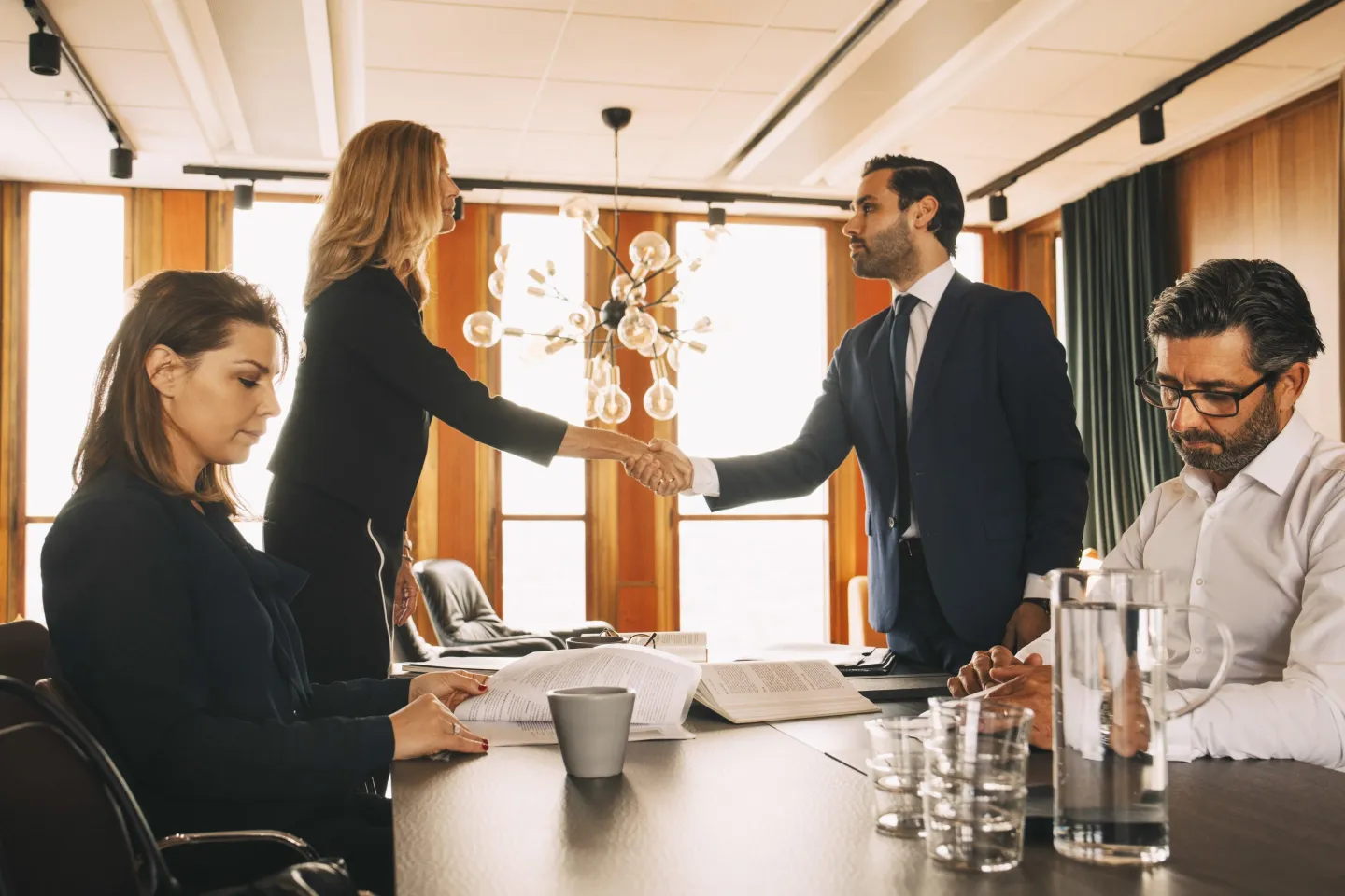 Male and female coworkers working while lawyers shaking hands at table in law office.