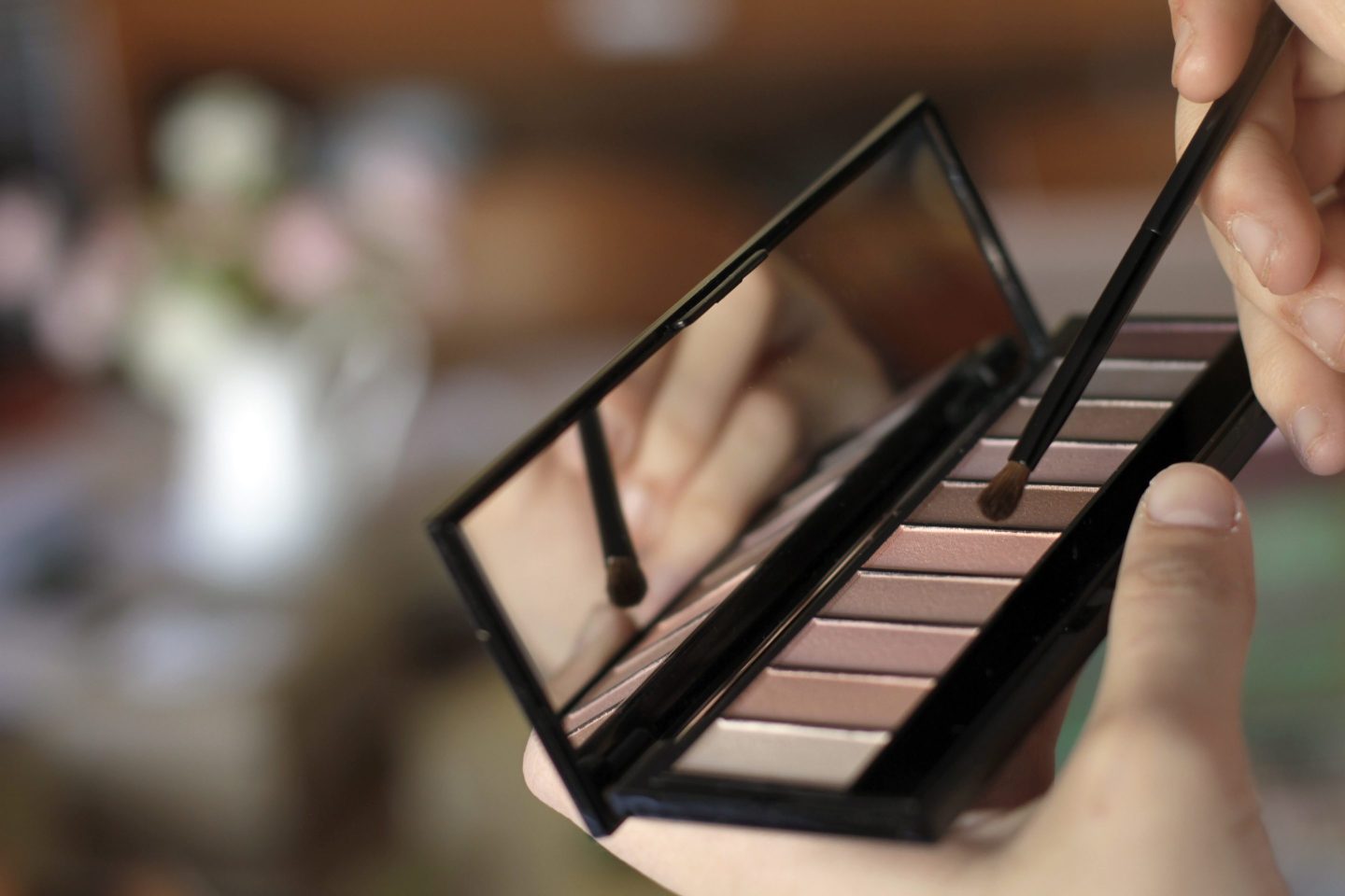 Close up of woman brushing with eye shadow pallet.