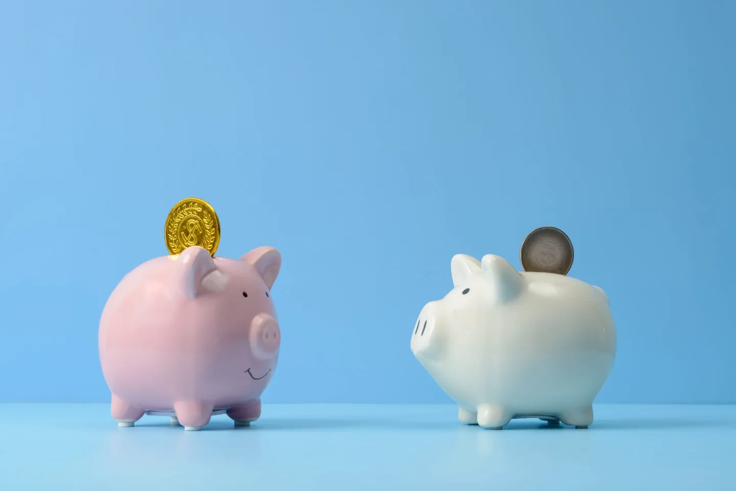 Silver coin and gold coin in two piggy banks.